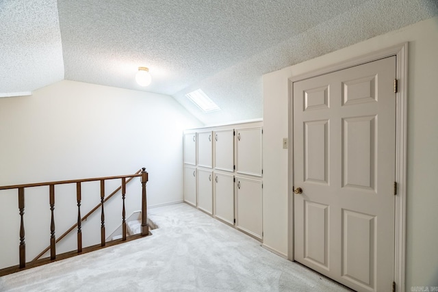 additional living space featuring vaulted ceiling with skylight, light colored carpet, and a textured ceiling