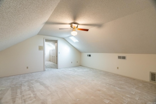 bonus room featuring vaulted ceiling with skylight, ceiling fan, light colored carpet, and a textured ceiling