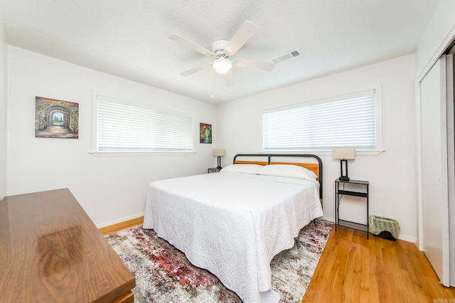 bedroom featuring a closet, light hardwood / wood-style flooring, multiple windows, and ceiling fan