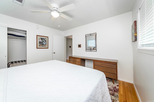 bedroom with a textured ceiling, a closet, wood-type flooring, and ceiling fan