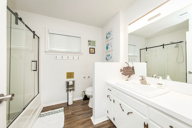 full bathroom featuring vanity, wood-type flooring, combined bath / shower with glass door, toilet, and a textured ceiling