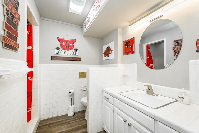 bathroom with vanity, toilet, hardwood / wood-style floors, and tile walls