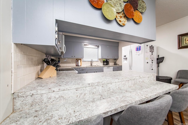 kitchen with a kitchen bar, white appliances, sink, gray cabinets, and decorative backsplash