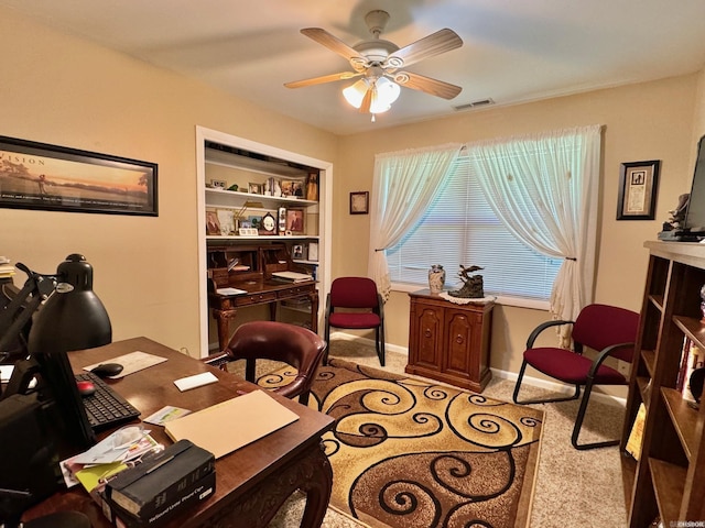 office space featuring built in shelves, ceiling fan, and light colored carpet