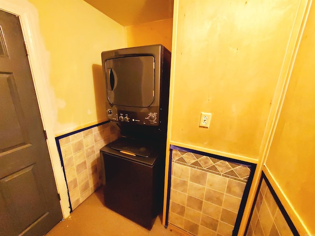 kitchen featuring a wainscoted wall, stacked washer and dryer, and tile walls