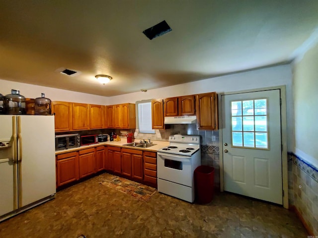 kitchen featuring under cabinet range hood, white appliances, a sink, tile walls, and brown cabinetry