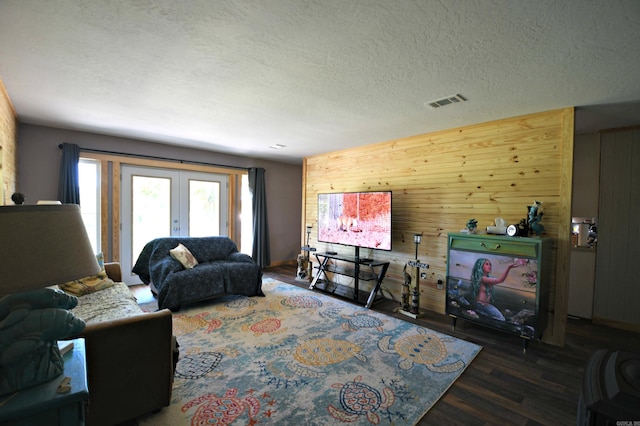 living room featuring dark hardwood / wood-style flooring, wooden walls, french doors, and a textured ceiling