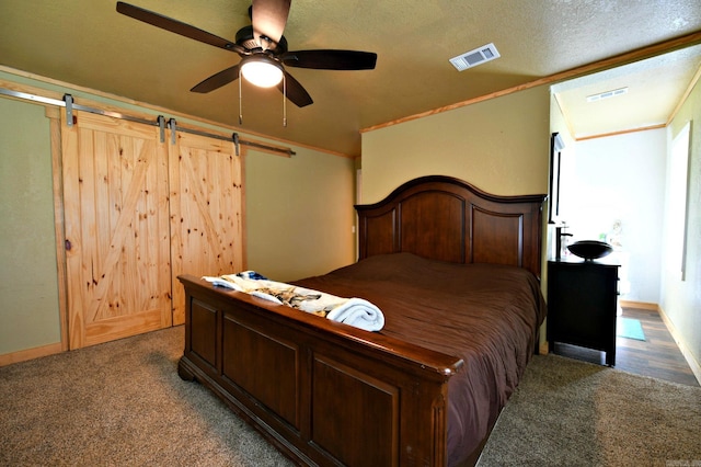 bedroom with a barn door, carpet flooring, visible vents, and a textured ceiling