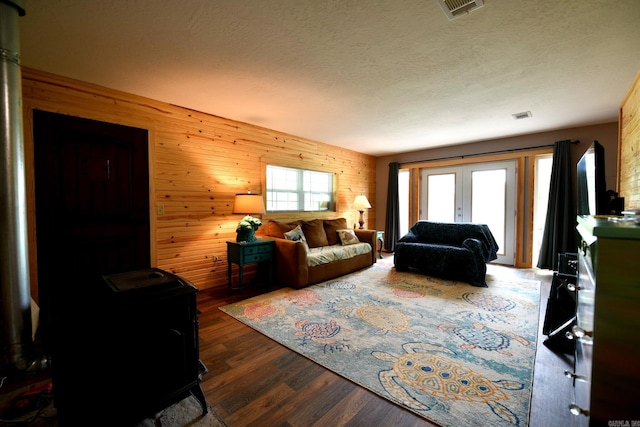 living area featuring visible vents, a textured ceiling, dark wood-style floors, french doors, and wood walls