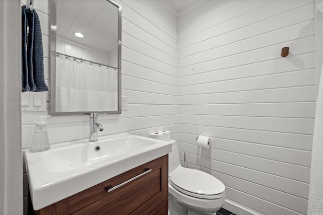 bathroom with wood walls, toilet, and vanity