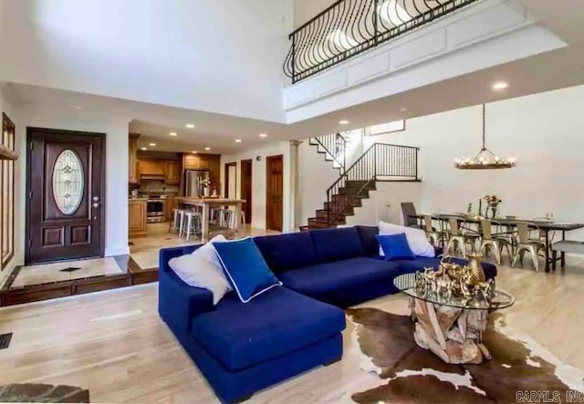 living room with a towering ceiling, a chandelier, and light hardwood / wood-style floors