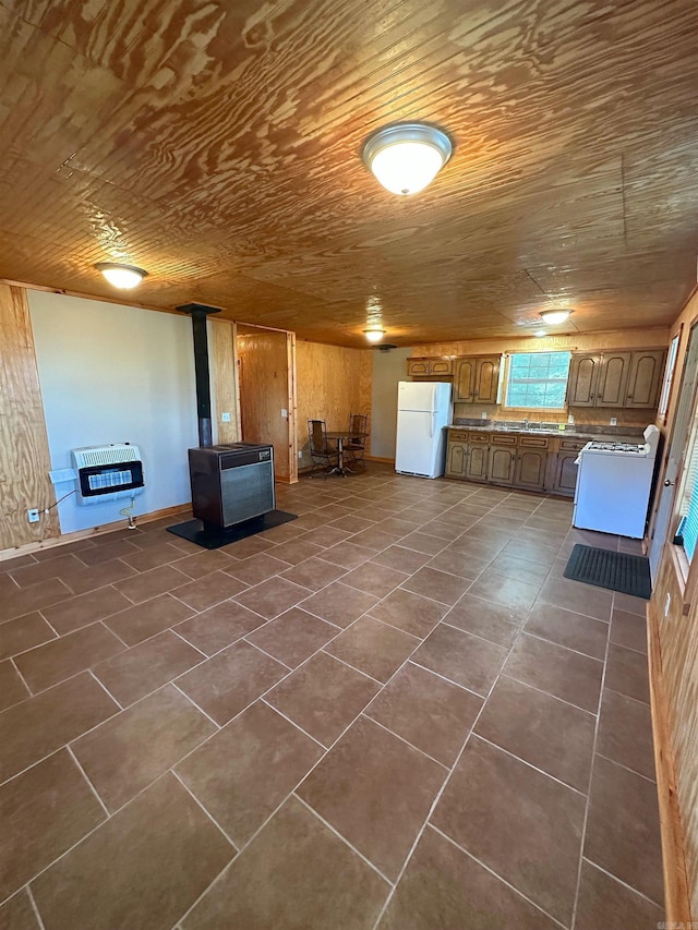 basement with heating unit, wooden walls, white refrigerator, wooden ceiling, and a wood stove