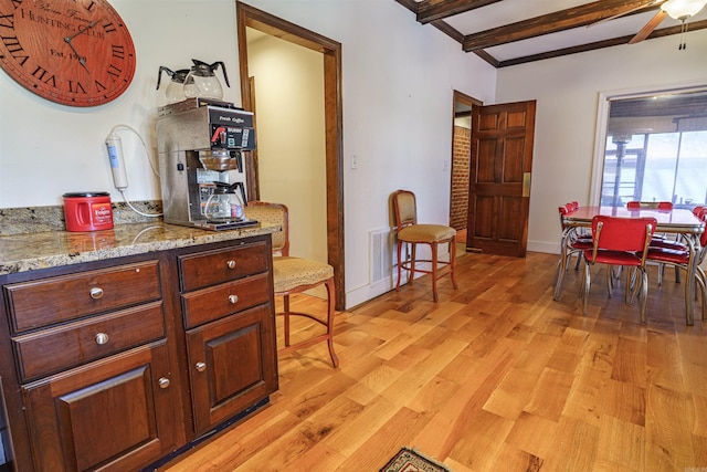 kitchen with beamed ceiling, light hardwood / wood-style floors, ceiling fan, and light stone counters