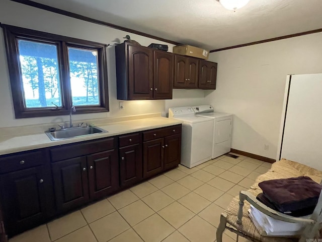 clothes washing area with sink, ornamental molding, light tile flooring, and washing machine and clothes dryer