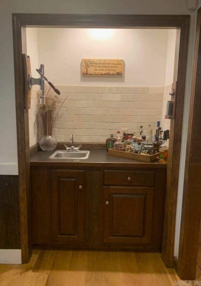 bar featuring dark brown cabinetry, sink, light hardwood / wood-style flooring, and backsplash