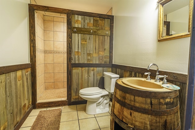 bathroom with tile flooring, a tile shower, wood walls, toilet, and vanity