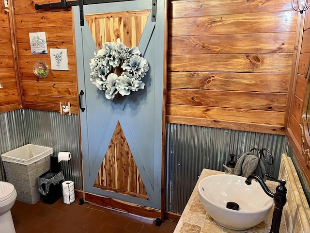 bathroom with tile patterned flooring, sink, wooden walls, and toilet