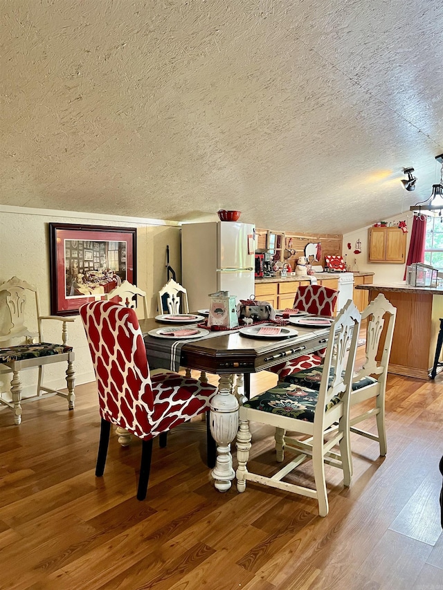 dining room with hardwood / wood-style flooring, vaulted ceiling, and a textured ceiling