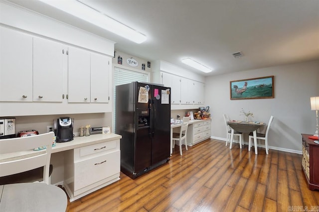 kitchen featuring black fridge, white cabinets, built in desk, and dark hardwood / wood-style floors