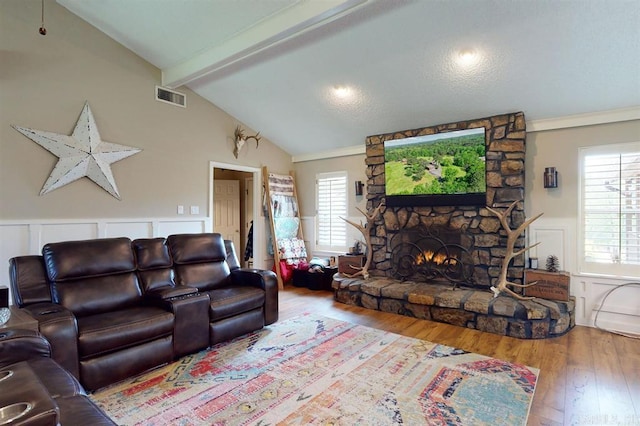 living room featuring vaulted ceiling with beams, a stone fireplace, and wood-type flooring