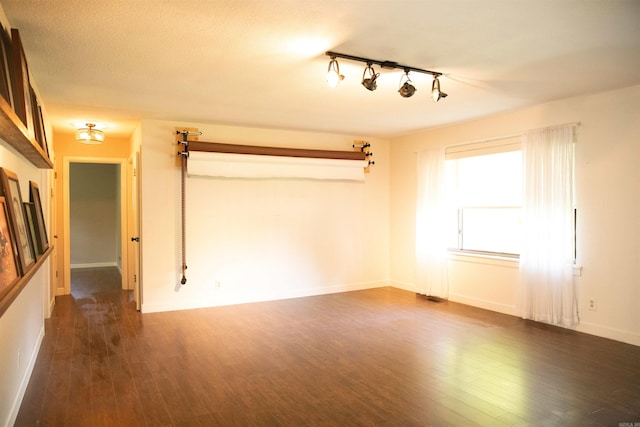 unfurnished room with dark hardwood / wood-style floors and rail lighting