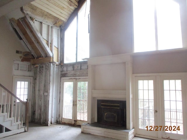 unfurnished living room with a wood stove, high vaulted ceiling, and french doors