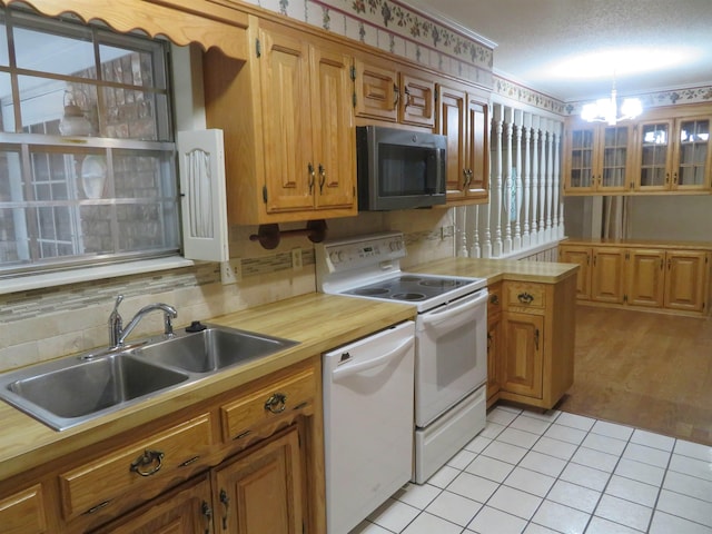 kitchen with light tile patterned flooring, sink, an inviting chandelier, hanging light fixtures, and white appliances