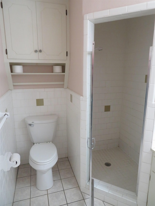 bathroom featuring tile patterned floors, toilet, a shower with door, and tile walls