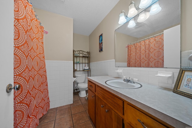 bathroom with toilet, a textured ceiling, tile walls, vanity, and tile patterned flooring