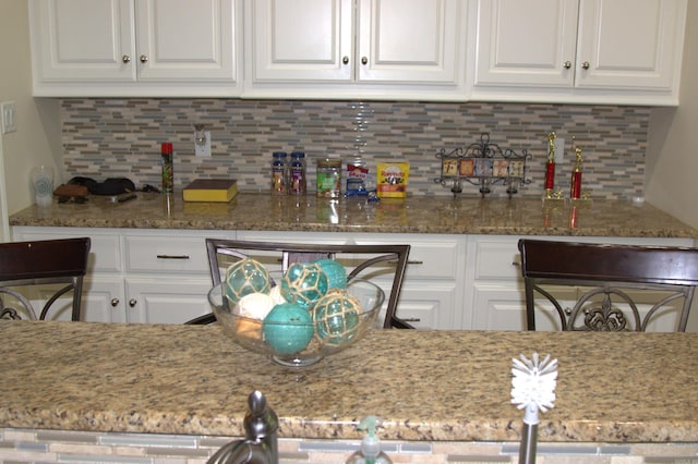 kitchen with backsplash, white cabinetry, and light stone counters