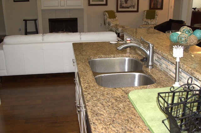 kitchen featuring a fireplace, dark hardwood / wood-style floors, light stone counters, and sink