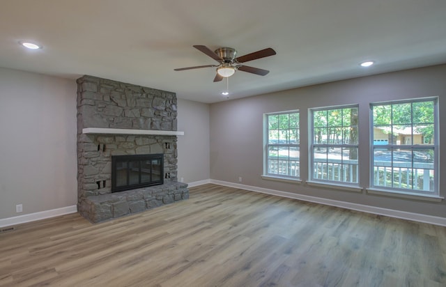 unfurnished living room with ceiling fan, a stone fireplace, and light wood-type flooring