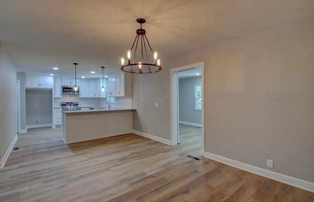 kitchen featuring light hardwood / wood-style flooring, appliances with stainless steel finishes, white cabinetry, tasteful backsplash, and kitchen peninsula