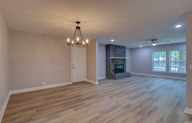 unfurnished living room featuring a fireplace, ceiling fan with notable chandelier, and light hardwood / wood-style flooring