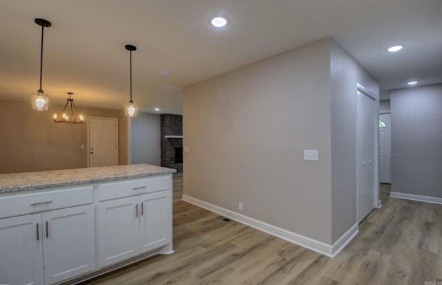 kitchen featuring white cabinetry, light stone counters, decorative light fixtures, and light hardwood / wood-style flooring