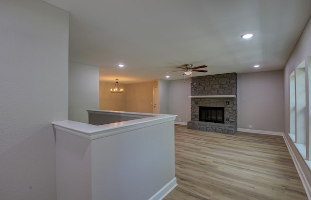 unfurnished living room with ceiling fan with notable chandelier, a fireplace, and light wood-type flooring