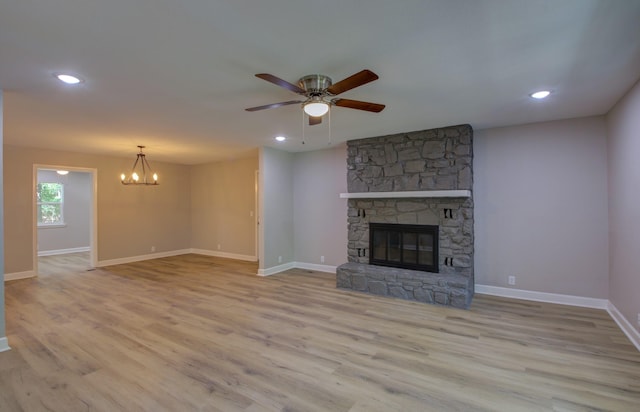 unfurnished living room with a fireplace, ceiling fan with notable chandelier, and light hardwood / wood-style flooring