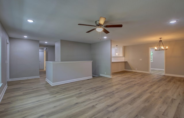 empty room with ceiling fan with notable chandelier and light hardwood / wood-style flooring