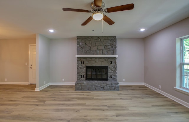 unfurnished living room with a stone fireplace, ceiling fan, and light wood-type flooring