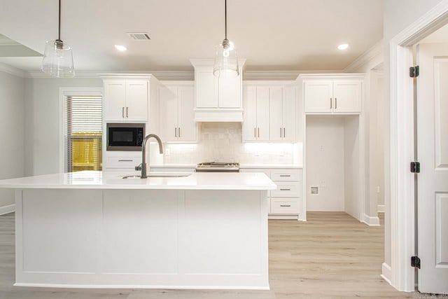 kitchen featuring built in microwave, a kitchen island with sink, sink, white cabinetry, and hanging light fixtures