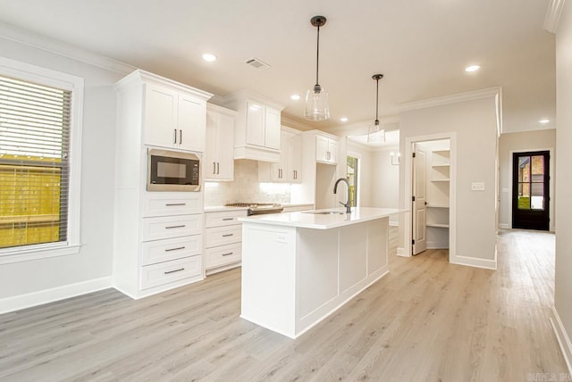 kitchen featuring white cabinetry, built in microwave, sink, an island with sink, and decorative light fixtures