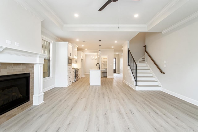 unfurnished living room featuring ceiling fan with notable chandelier, a tray ceiling, sink, light hardwood / wood-style flooring, and a fireplace