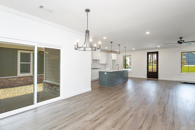 interior space featuring a center island with sink, ceiling fan with notable chandelier, hanging light fixtures, tasteful backsplash, and white cabinetry