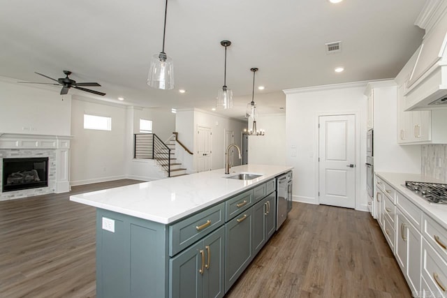 kitchen with sink, pendant lighting, a premium fireplace, white cabinetry, and an island with sink