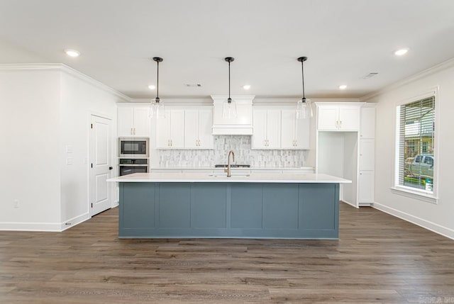 kitchen with white cabinets, decorative light fixtures, built in microwave, and a kitchen island with sink