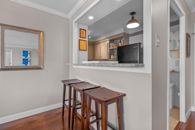 kitchen featuring ornamental molding, black fridge, wood-type flooring, and a kitchen bar