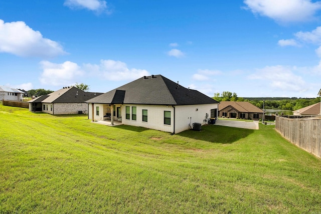 rear view of house with a yard, fence, central air condition unit, a patio area, and a shingled roof