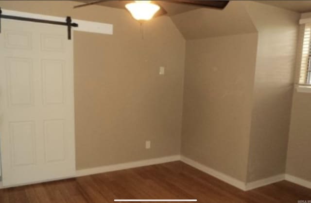 spare room with dark wood-type flooring, ceiling fan, and a barn door