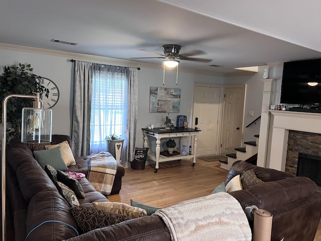 living room featuring hardwood / wood-style flooring, ceiling fan, a fireplace, and crown molding