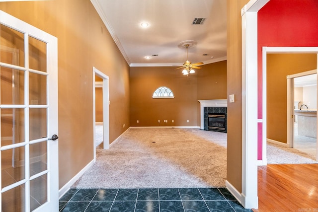 unfurnished living room featuring crown molding, ceiling fan, a premium fireplace, and dark colored carpet